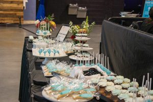 A long, black table features a spread of baby blue and white desserts