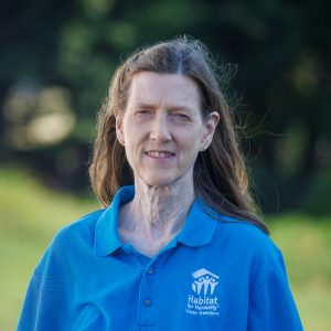 A brown-haired woman smiles at the camera while wearing a Habitat Greensboro blue polo t-shirt.