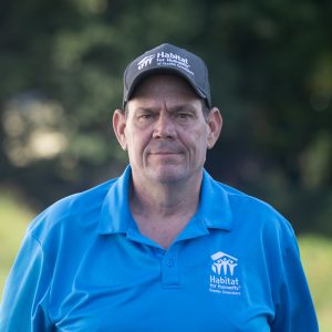 A man smiles at the camera while wearing a Habitat Greensboro grey ball cap and blue polo t-shirt.