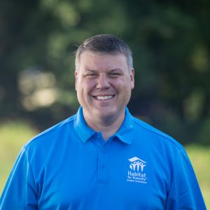 A man with short, brown-and-grey hair smiles at the camera while wearing a Habitat Greensboro blue polo t-shirt.