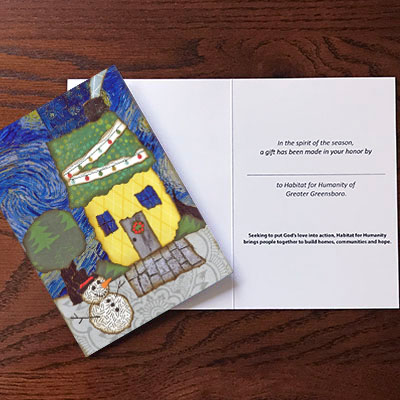 The front and interior of a 2024 Habitat Greensboro Holiday Card. The front shows an artist's rendition of a yellow house with a green roof in the snow. The interior features a blank line where one can designate the recipient of the card.